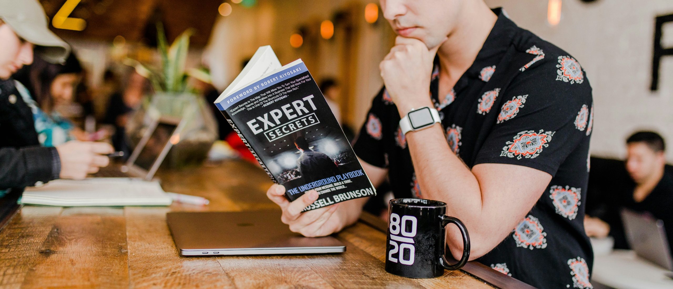 An image of a young man reading a book titled Expert Secrets.